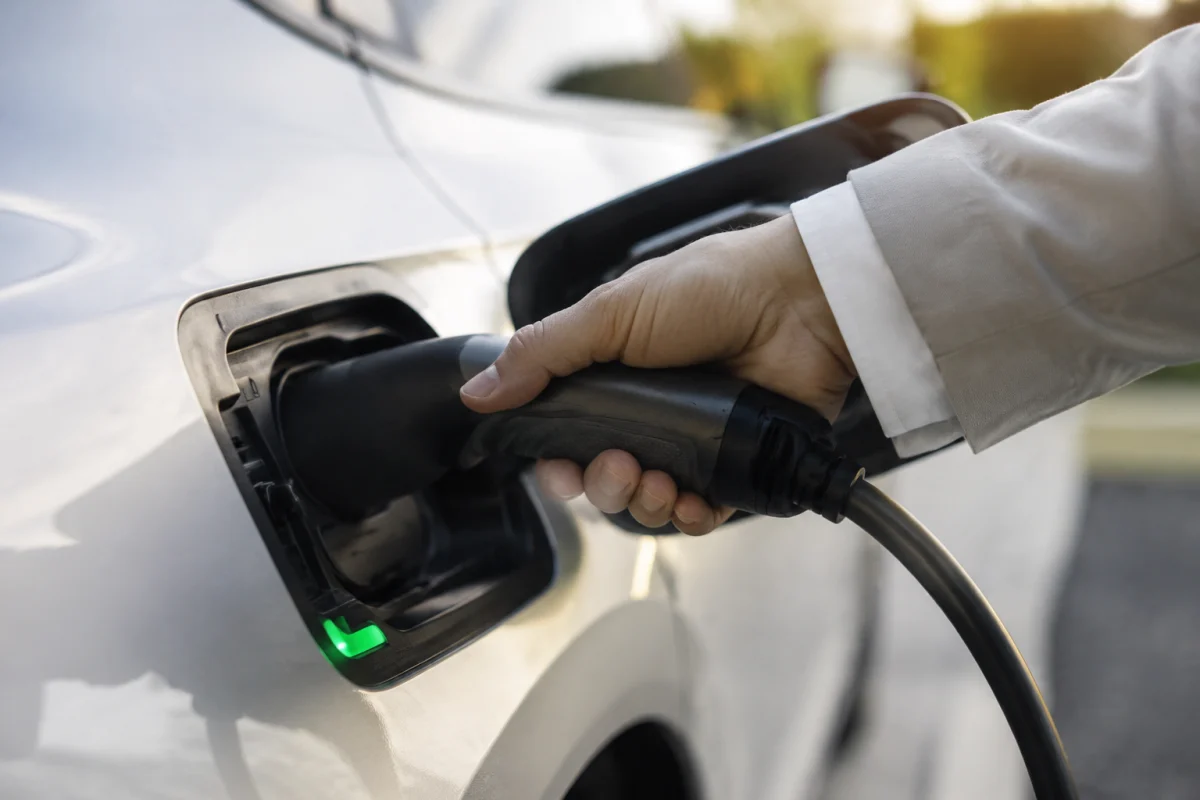 Gros plan sur un connecteur de recharge inséré dans la prise d'une voiture électrique blanche garée en entreprise