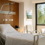 Vue d'ensemble d'une chambre individuelle d'hôpital moderne avec lit médicalisé et fenêtre lumineuse
