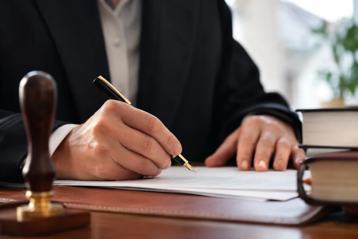 Gros plan sur une main signant un acte de notoriété posé sur un bureau en bois